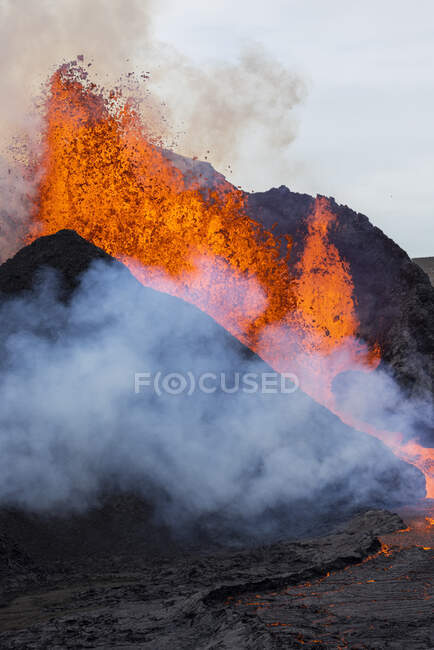 Schizzi di lava arancione calda che eruttano dalla vetta vulcanica circondata dal fumo in Islanda — Foto stock