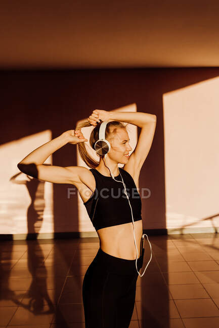 Молодая атлетичная белая женщина, завязывающая хвостик во время тренировки на закате, тени и свет на заднем плане — стоковое фото