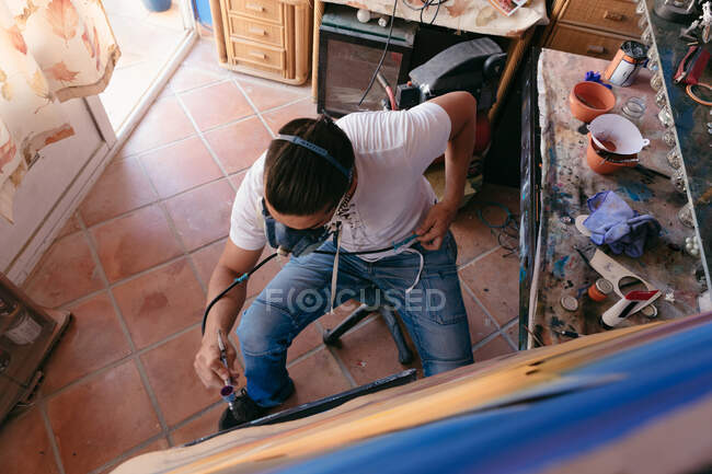 Von oben männliche Künstler in Atemschutzmaske mit Spritzpistole, um Bild auf Leinwand während der Arbeit in der kreativen Werkstatt malen — Stockfoto