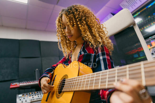 From below young African American female guitarist with classical guitar sitting in studio — Stock Photo