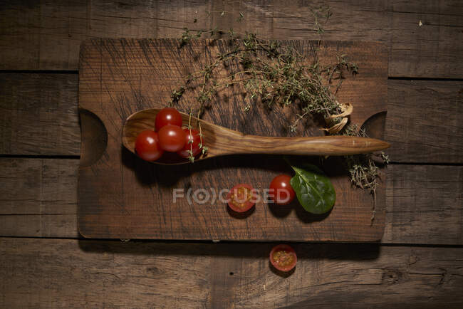 Top view composition of fresh ripe red cherry tomatoes with aromatic basil leaf and bunch of thyme on wooden cutting board with spoon — Stock Photo