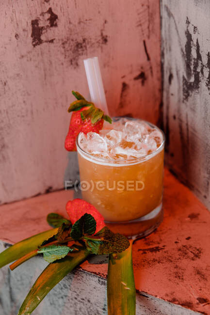 High angle of San Francisco cocktail made of vodka liquor and orange juice garnished with strawberry and ice cubes placed on palm leaves — Stock Photo