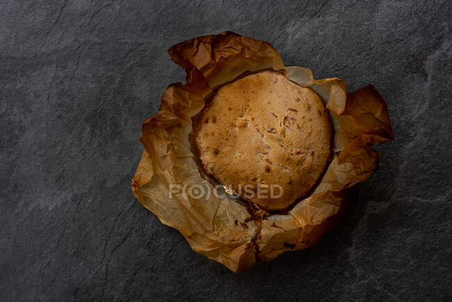 Vista dall'alto del pane rotondo artigianale appena sfornato con crosta croccante su carta pergamena posta su fondo nero — Foto stock
