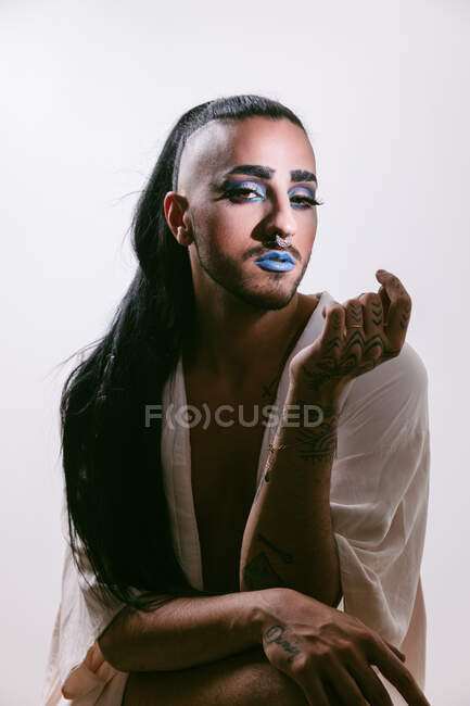 Portrait of glamorous transgender bearded woman in sophisticated make looking at camera against neutral background — Stock Photo