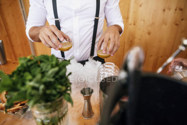 Alto ángulo de cultivo camarero irreconocible en uniforme que sirve bebidas alcohólicas en la mesa durante el evento festivo - foto de stock