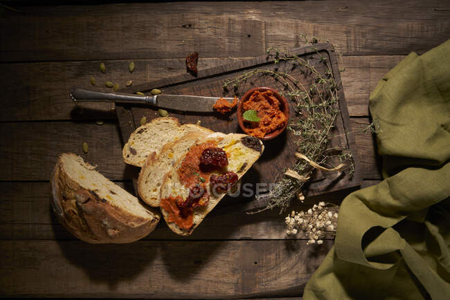 De cima de apetitosas fatias de pão caseiras frescas com tomates secos ao sol e ervas aromáticas na mesa de madeira rústica — Fotografia de Stock