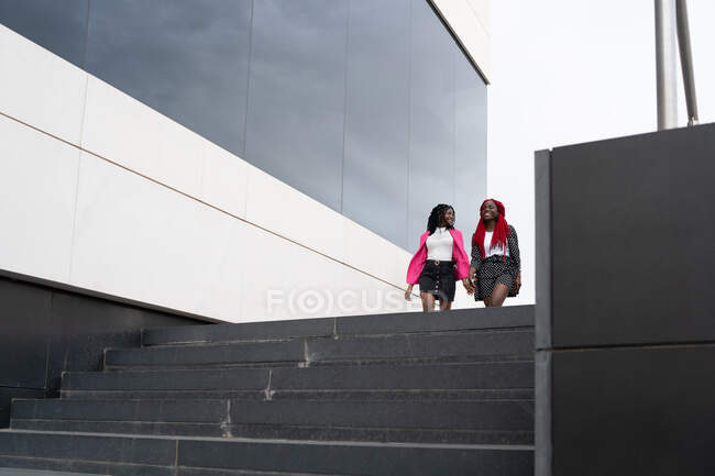Ground level full body of African American women in stylish wear doing runway walk together near modern building — Stock Photo