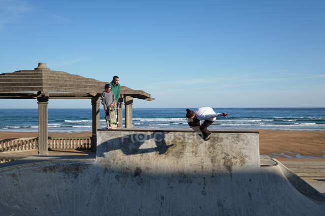 Patineurs actifs chevauchant des planches à roulettes et montrant des astuces dans le skate park au bord de la mer en été — Photo de stock
