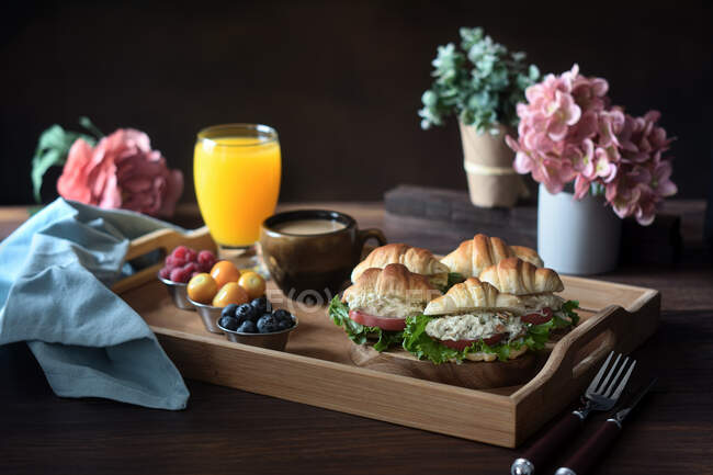 Delicious croissant sandwiches with vegetables served on tray with cappuccino and orange juice prepared for French breakfast and placed on wooden table — Stock Photo