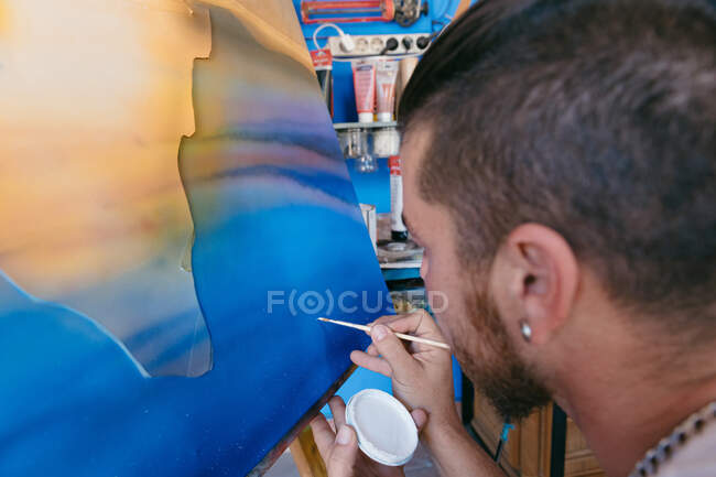 Бородатый человек рисует точки с белым пигментом на холсте с абстрактной картиной во время работы в творческой мастерской — стоковое фото