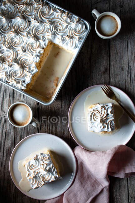 D'en haut trois laits gâteau dans un plat de cuisson et des assiettes avec des tasses de café fort sur une table en bois — Photo de stock