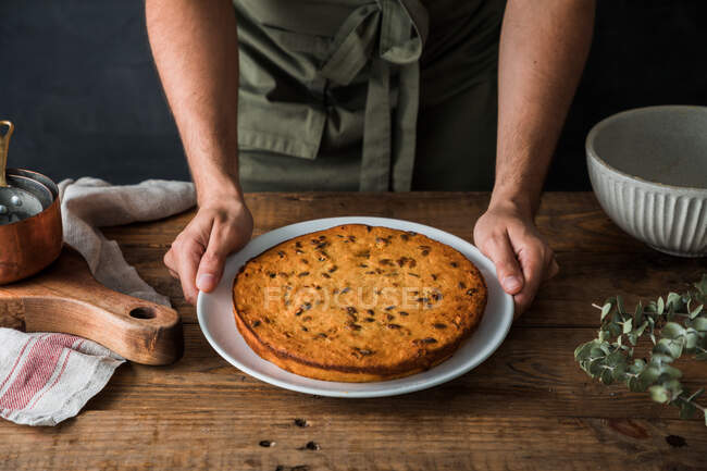 Cropped anônimo cozinheiro masculino segurando prato com deliciosa torta de abóbora na mesa de madeira — Fotografia de Stock