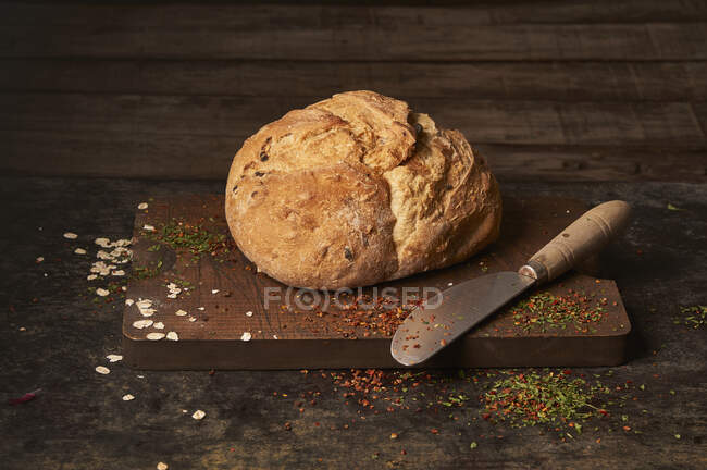 Antipasto aromatico appena sfornato pane fatto in casa con uvetta posta su tavola di legno cosparsa di erbe aromatiche — Foto stock