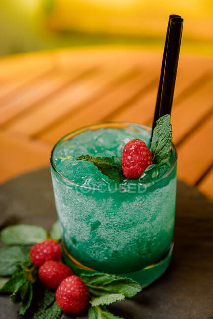 Grand angle de cocktail exotique à base de gin aux fruits de la passion mélangés avec du jus de citron et du curaçao bleu servi avec des feuilles de baies et de menthe — Photo de stock