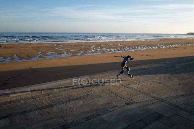 Jovem ativo masculino equitação skates ao longo promenade no fundo do mar e pôr do sol céu — Fotografia de Stock