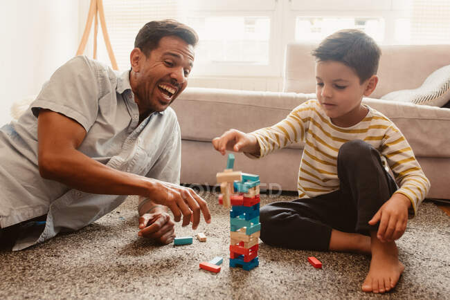 Вид сбоку отца и сына, играющих со строительными деталями в столовой дома — стоковое фото