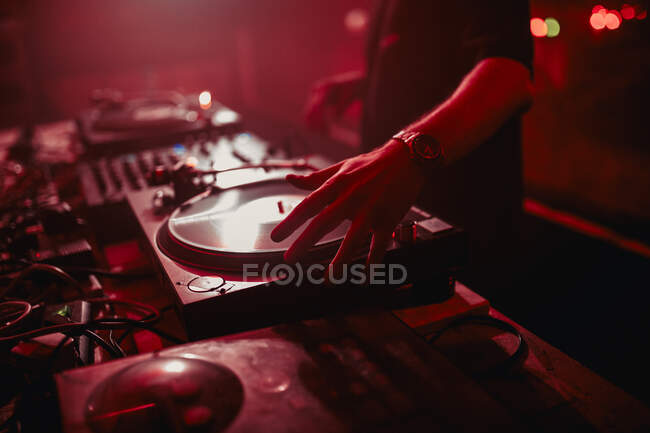 Side view of crop male DJ mixing music on controller during concert in dark nightclub — Stock Photo