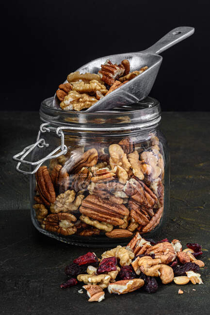 Glasgefäß mit Nüssen und Trockenfrüchten auf dunklem, rustikalem Hintergrund — Stockfoto