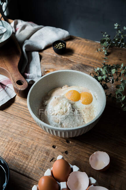 De arriba cuenco con huevos y crema mezclados con migas de pan y harina en la mesa de madera durante la preparación de la repostería - foto de stock