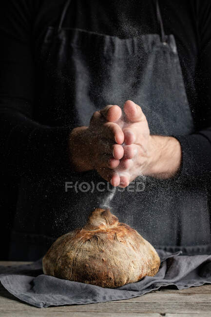 Chef méconnaissable dans un tablier debout à table et décorer pain traditionnel avec de la farine — Photo de stock