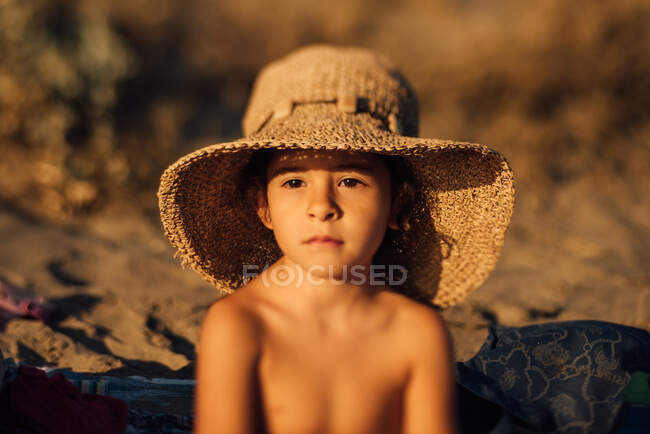 Nettes kleines Mädchen mit Strohhut lächelt glücklich, während es sich an einem sonnigen Sommertag am Strand ausruht — Stockfoto