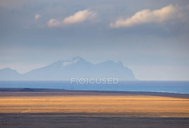 Рівнина сухий берег і спокійне блакитне море, розташоване на далекому гірському хребті в хмарний ранок в Ісландії — стокове фото