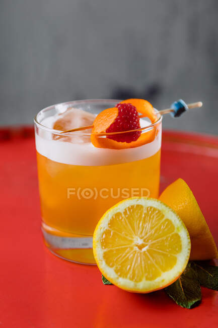 Crystal glass of Amaretto Sour cocktail garnished with orange zest and raspberry served with halved lemon — Stock Photo