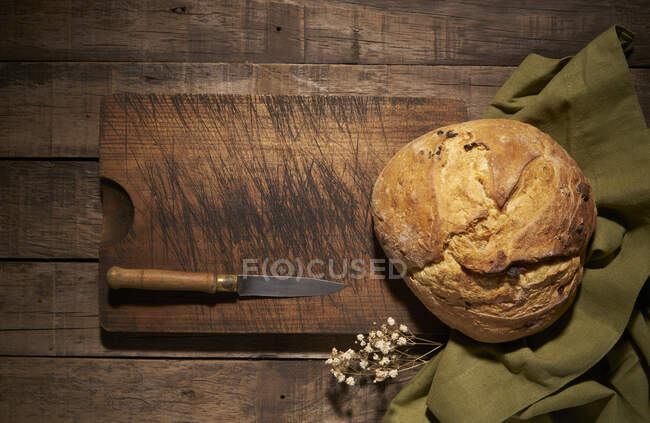 Зверху цілий круглий свіжоспечений хлібний хліб з хрусткою скоринкою, розміщений на дерев'яній обробній дошці з ножем на сільському столі — стокове фото