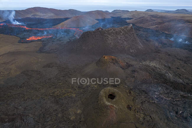 Вид беспилотника на поток горячей апельсиновой лавы, протекающей по горной местности утром в Исландии — стоковое фото