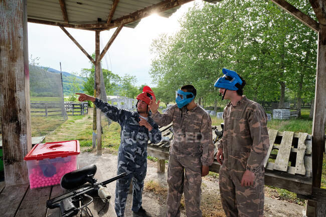 Empresa de jogadores do sexo masculino em máscaras e roupas de camuflagem se preparando para jogar paintball — Fotografia de Stock