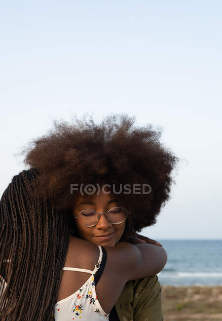 Счастливые молодые афро-американские подруги обнимают друг друга, проводя вместе летние каникулы на берегу моря — стоковое фото