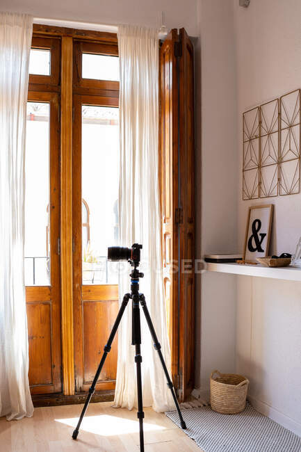 Cámara de fotos moderna en trípode colocado en la habitación de acogedor apartamento con luz solar - foto de stock