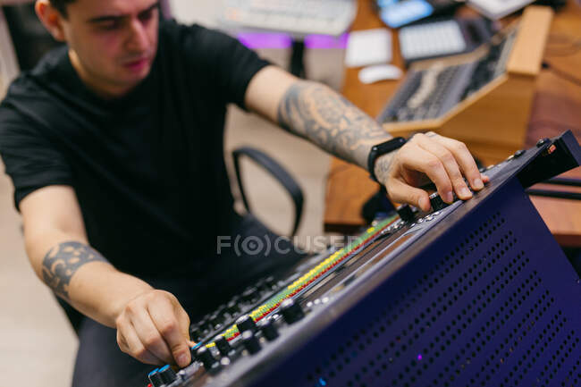 Vista lateral de corte tatuado engenheiro de som masculino trabalhando com painel de controle em placa de áudio em estúdio de gravação — Fotografia de Stock