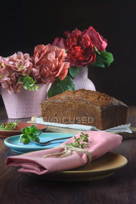 Nature morte d'un gâteau éponge à côté de vases roses avec des fleurs sur une table — Photo de stock
