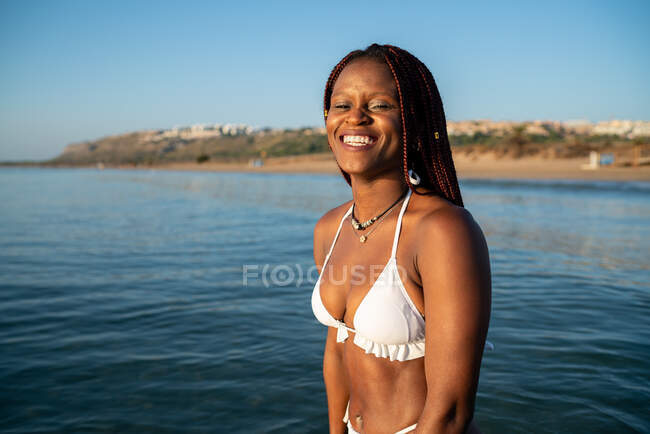 Femme noire avec des tresses sur la plage souriant et regardant la caméra — Photo de stock
