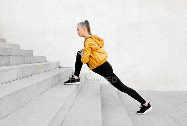 Joven atlética mujer caucásica estirándose al aire libre cerca de escaleras - foto de stock