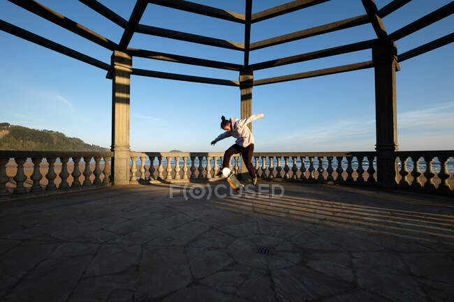 Динамічний чоловічий фігурист стрибає зі скейтбордом на плитці на терасі на заході сонця влітку і виконує трюк — стокове фото