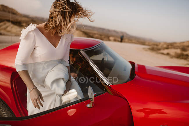 Noiva e noivo descansando perto de veículo vermelho de luxo durante a viagem através do Parque Natural Bardenas Reales de manhã em Navarra, Espanha — Fotografia de Stock