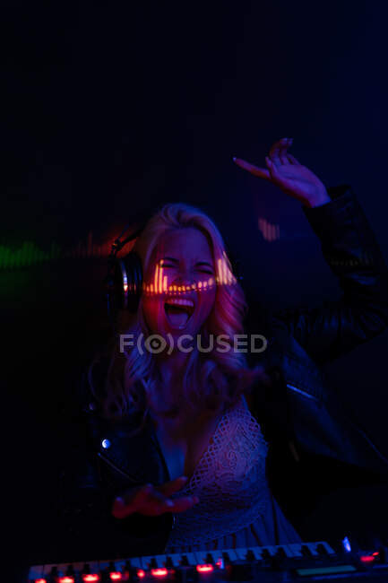 Счастливая женщина поднимает руку и кричит от волнения, играя музыку во время вечеринки в темном ночном клубе — стоковое фото