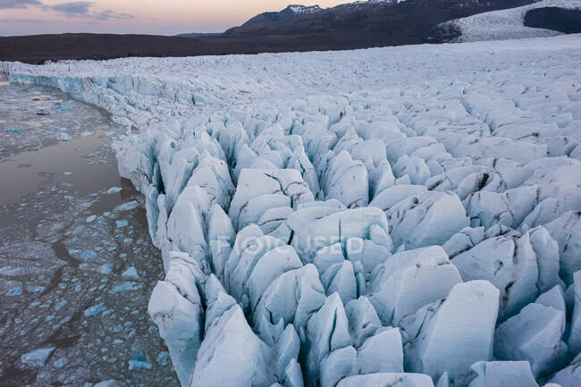 Сверху беспилотник видит льдины, плавающие в холодной морской воде около грубого ледника зимой в Исландии — стоковое фото