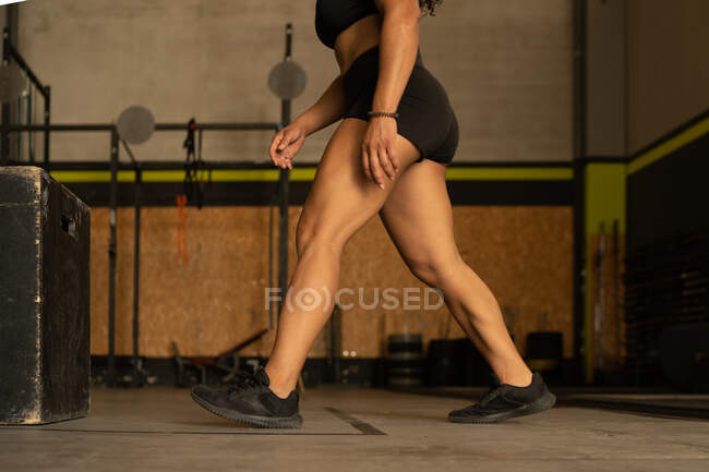 Vista lateral nível do solo de atleta feminina forte em activewear andando no ginásio durante o treinamento — Fotografia de Stock