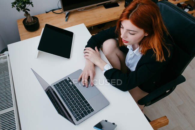 Зверху молода жінка-підприємець працює на нетбуці за столом з планшетом і смартфоном вдома — стокове фото