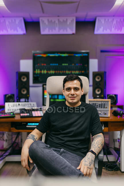 Confident male sound engineer sitting with crossed legs in armchair while looking at camera in recording studio — Stock Photo