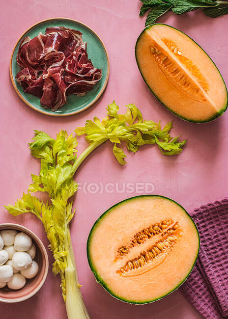 Dall'alto melone esotico, mozzarella e prosciutto ingredienti per la preparazione di insalata su sfondo rosa colorato — Foto stock