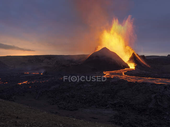 Salpicaduras de lava naranja caliente en erupción desde el pico de la montaña volcánica rodeado de humo en Islandia - foto de stock