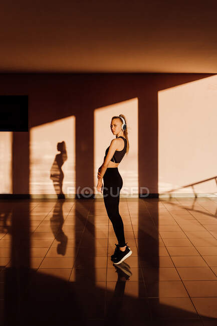 Молода атлетична біла жінка слухає музику із закритими очима та розслабляється на заході сонця, тіні та світло на фоні — стокове фото