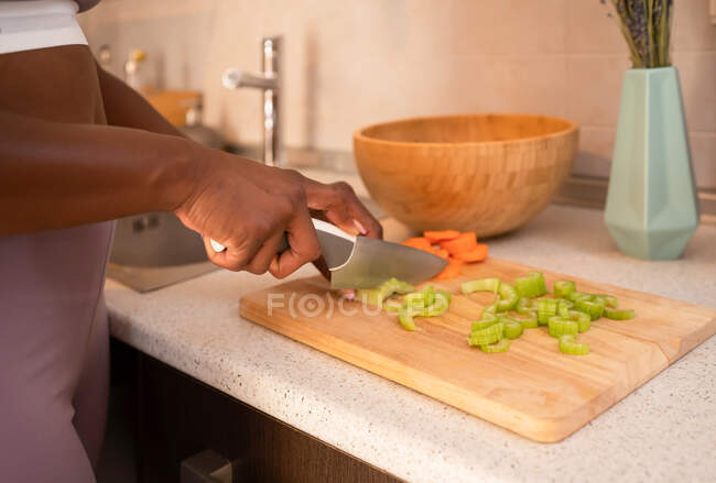 Crop unrecognizable ethnic female cutting fresh vegetables on chopping board while cooking tasty salad for lunch at home — Stock Photo