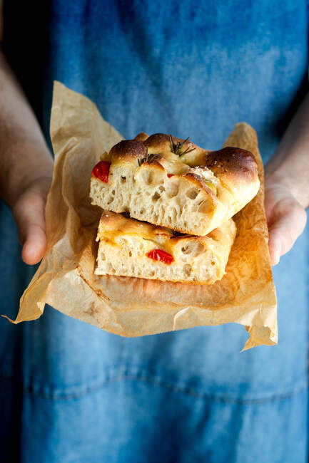 Crop person hands holding piece of fresh tomato focaccia with rosemary — Stock Photo