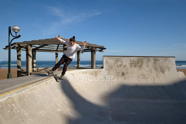 Неузнаваемый юноша катается на скейтборде в скейт-парке в солнечный день на берегу моря — стоковое фото