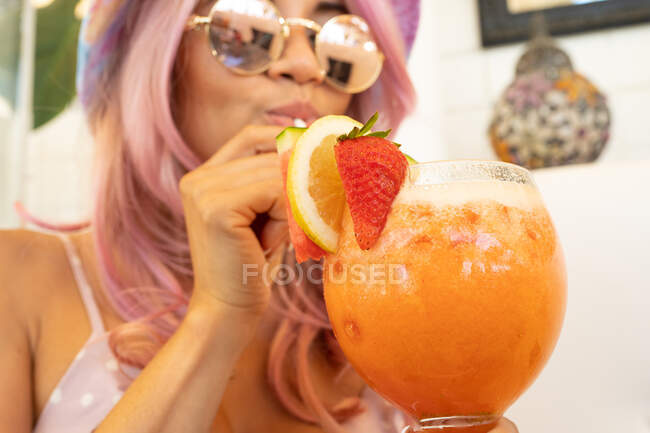 Conteúdo fêmea com cabelo rosa e roupa de verão bebendo coquetel laranja doce com frutas durante as férias — Fotografia de Stock
